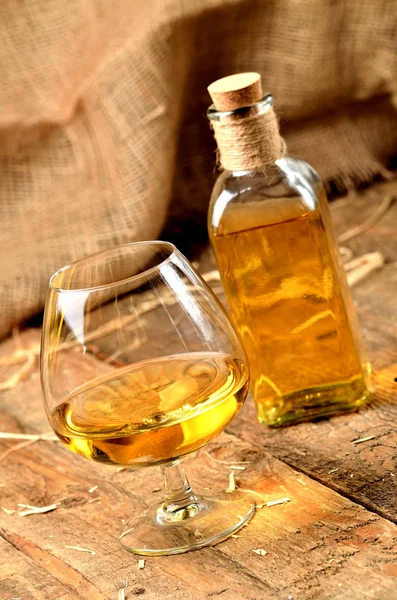 Gelas cognac pada latar belakang kayu dan botol di latar belakang — Stok Foto
