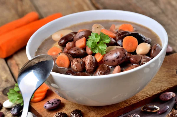 Detail of bowl of bean soup with large beans , spoon, carrots, parsley and marjoram — Stock Photo, Image