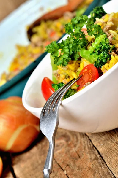 Nahaufnahme von Gabel und Thunfisch-Risotto mit Gemüse, Tomaten, Brokkoli und Petersilie in der Schüssel, Zwiebeln und Pfanne im Hintergrund — Stockfoto