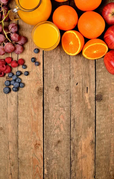 Sumo de laranja, laranjas frescas, maçãs, uvas, framboesas e mirtilos em uma mesa de madeira - fundo de fruto - visão de cima - foto vertical — Fotografia de Stock