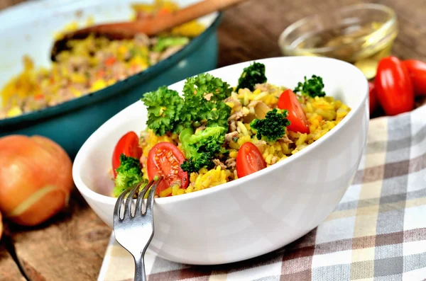 Nahaufnahme von Gabel und Thunfisch-Risotto mit Gemüse, Tomaten, Brokkoli und Petersilie in der Schüssel, Zwiebeln, Öl und Pfanne im Hintergrund — Stockfoto