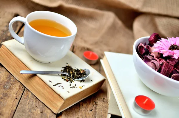 Tazza di tè nero e cucchiaio con tè sciolto su un vecchio libro squallido vintage, candela e fiori secchi sullo sfondo — Foto Stock