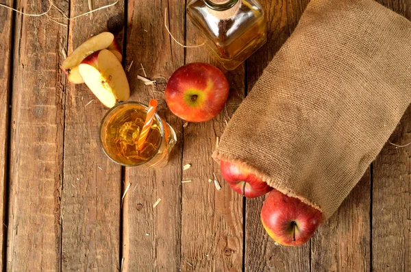 Vue d'en haut du jus de pomme fait maison avec glace, pommes rouges, paille, nature morte sur une table en bois — Photo