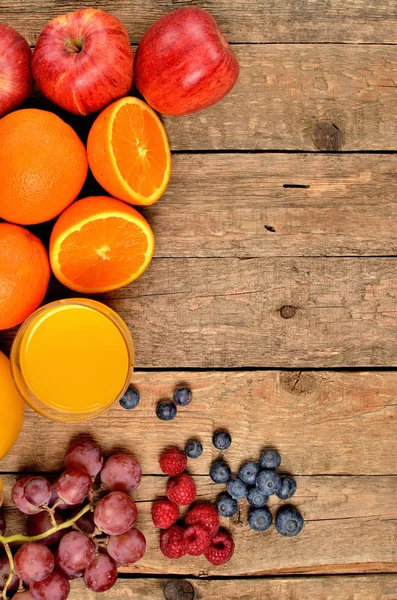 Jugo de naranja, naranjas frescas, manzanas, uvas, frambuesas y arándanos en una mesa de madera - vista desde arriba - foto vertical - marco de orientación izquierda — Foto de Stock