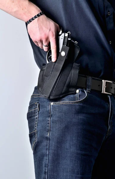Närbild av mans hand att dra ut en pistol pistol från hölster på bältet, blå jeans, svart tröja — Stockfoto
