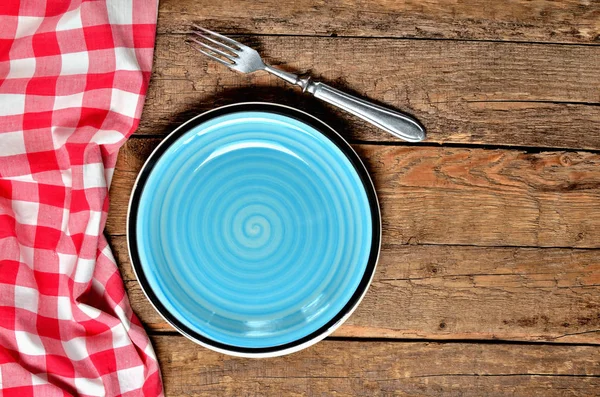 Seramik tabak, çatal, halka ve eski vintage ahşap masa arka plan üzerinde kırmızı kareli masa örtüsü sol çerçeve mavi - yukarıdan görüntüleyin — Stok fotoğraf