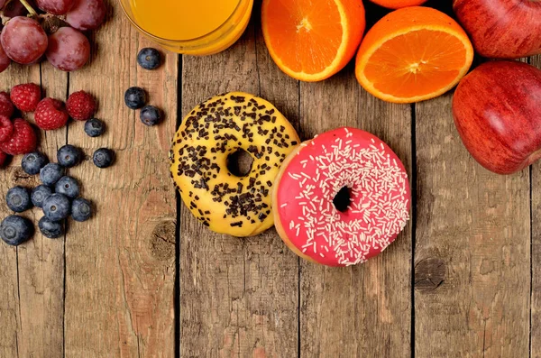 Donuts, blueberries, raspberries, apples, oranges - sweet breakfast on wooden table - view from above — Stock Photo, Image