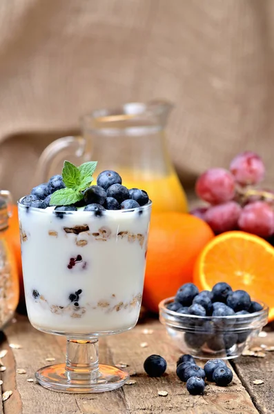 Joghurt mit Haferflocken, frischen Blaubeeren und Minzblättern sowie Orangen und Trauben im Hintergrund — Stockfoto