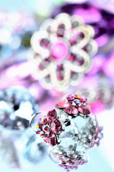 Close-up of red flower shaped earrings with red diamonds and big rounded gold brooch jewelery - reflection effect - colored backgrounds - purple - cold color balance - vertical photo — Stock Photo, Image