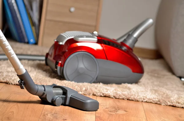 Vacuum cleaner on floating floor and shaggy carpet, desk with files and sofa in background