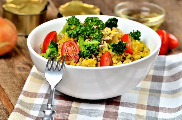 Nahaufnahme von Gabel und Thunfisch-Risotto mit Gemüse, Tomaten, Brokkoli und Petersilie in der Schüssel, Zwiebeln, Dosen und Öl im Hintergrund — Stockfoto