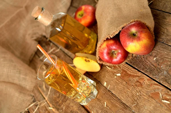 Jus apel, apel merah, jerami dan botol di latar belakang pada papan kayu pedesaan — Stok Foto