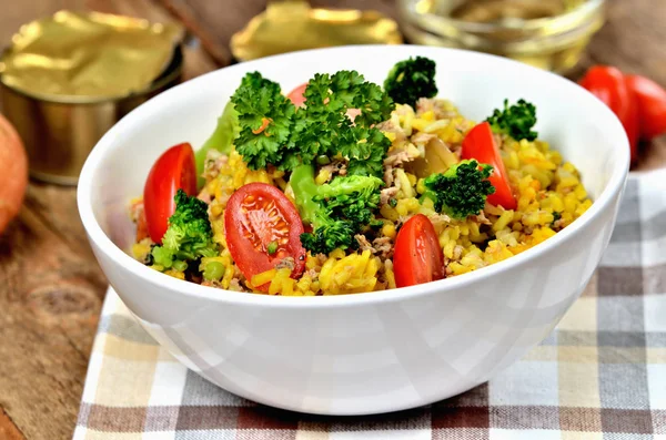 Nahaufnahme von Thunfisch-Risotto mit Gemüse, Tomaten, Brokkoli und Petersilie in der Schüssel, Zwiebeln, Dosen und Öl im Hintergrund — Stockfoto