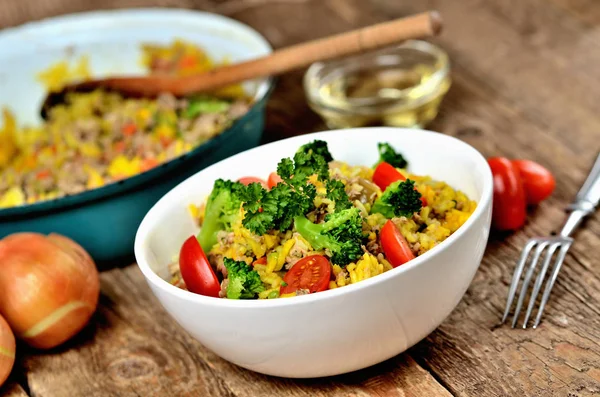 Schüssel mit Thunfisch-Risotto mit Gemüse, Tomaten, Brokkoli und Petersilie, Zwiebeln und Öl im Hintergrund — Stockfoto