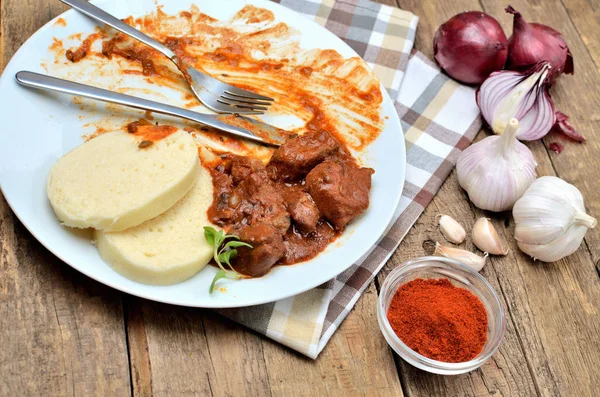 Jedzenie mięsa wieprzowego gulasz z kluskami na sztućce, czosnek, cebula, pieprz, białe płytki, obrus w tle - typowy czeski żywności — Zdjęcie stockowe