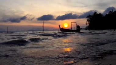 Tayland ve motorlu uzun kuyruklu teknelerin silueti gün doğumunda dalgaların üzerinde yuvarlanır.