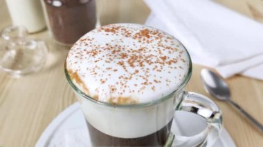 Kapuçino ya da fincanda latte. Beyaz köpüklü süt üzerine tarçın ve kakao tozu serpilmiştir. Tatlı içeceği süslemesi. Uzun, berrak bardakta, çırpılmış kremalı hazır kahve. Yakın plan.