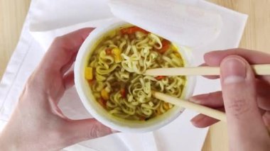 Bardaktaki yumurtalı erişte çubukla karıştırılır. Anında ramen çorbası. Tavuk aromalı fast food, kurutulmuş havuç, mısır. Yakın tepe, ahşap masa, beyaz peçete, 4k