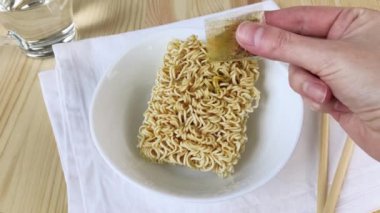 Çuvaldan baharat serpiştirilmiş erişteli yumurta. Anında ramen çorbası. Evde fast food pişirmek, kasede bir parça kuru erişte. Yakın plan, ahşap masa, beyaz peçete, çubuklar, 4k.