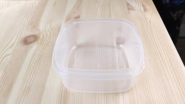 Atık ayıklama. Plastik şişe kapakları. Beyaz eller çok renkli kapakları konteynıra koyuyor. Doğanın bilinçli bakımı, çöpler, çöpleri geri dönüşüm için kullanmak. Tahta masa.