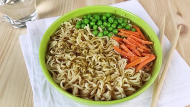 新鮮なエンドウ豆とニンジンと緑のプレートのラーメンスープ スープや野菜と卵麺に塩を振りかける 自宅で心のこもった昼食を調理します 閉じて 木製のテーブル 白いナプキン — ストック動画