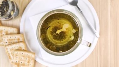 Yaseminli yeşil çay demlenir, yapraklar daireler çizer. Bardakta şeffaf bardakta sıcak içecek. Sağlıklı hafif kahvaltı. Yakın çekim üst manzara, ahşap masa, beyaz tepsi, kuru kurabiye.