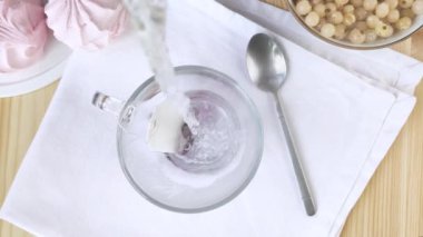 Meyve çay poşeti kaynar suyla demlenir. Cam şeffaf bardakta Hibiscus. Bardakta parlak kırmızı bir içecek. Şeker ve böğürtlenli yaz tatili. Yakın çekim üst manzara, beyaz peçete, lokum, frenk üzümü.