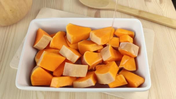スライスしたカボチャは油で水をやります 白い長方形の皿の中でオレンジ焼きカボチャを調理 健康的な野菜 菜食主義者のための食品 木製のテーブル — ストック動画