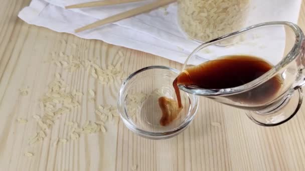 酱油在透明玻璃杯肉汁船上 亚洲菜的传统配料 木制餐桌 分散的米粒 白餐巾 — 图库视频影像