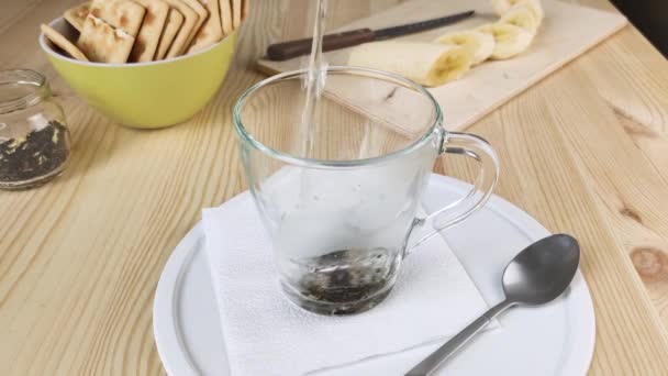 用茉莉花泡绿茶 用开水煮 热饮在透明玻璃杯中 健康的清淡早餐特写 木制桌子 白色盘子 干饼干和香蕉为背景 — 图库视频影像