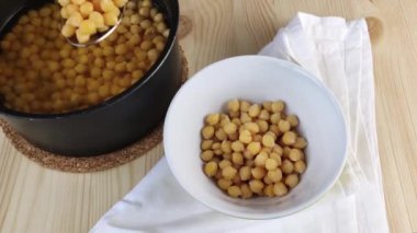 Haşlanmış nohutlar tavadan kaseye kaşıkla konur. Yakın plan, sağlıklı yemekler, ahşap masa.