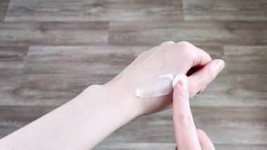 Krema beyaz kadın ellerine sürtünüyor. Nemlendirici cilt losyonu, ev bakımı, hidrasyon. Manikürsüz doğal tırnaklar. Yakın plan, ahşap arkaplan