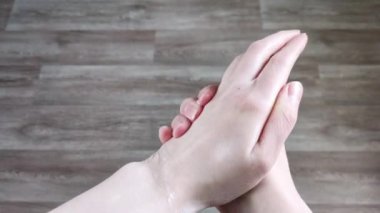Krema beyaz kadın ellerine sürtünüyor. Nemlendirici cilt losyonu, ev bakımı, hidrasyon. Manikürsüz doğal tırnaklar. Yakın plan, ahşap arkaplan