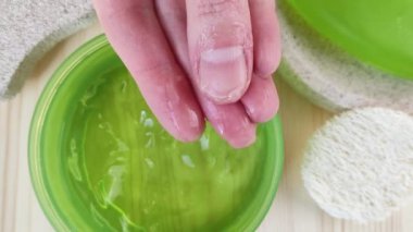 Yeşil kavanozda nemlendirici aloe jeli. Renksiz vücut losyonu ya da krem. Manikürsüz beyaz kadın elleri, yakın plan, yüzü olmayan, tahta masa. Doğal kozmetik ürünleri, ev cilt bakımı