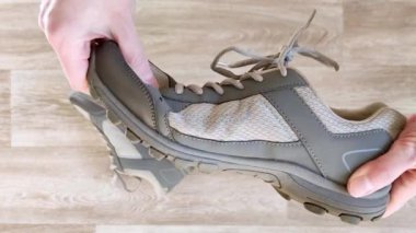 Beyaz eller gri ayakkabıyı sıkıyor. Spor ayakkabılarının lastik taban esnekliğini test edin. Yakın plan, ahşap arka plan, meçhul
