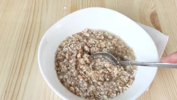 Le porridge brassé dans l'eau est mélangé avec une cuillère. Flocons de 4 céréales dans un bol blanc, seigle, blé, orge, avoine. Cuisson d'aliments sains, porridge de cuisson rapide pour le petit déjeuner. Gros plan, table en bois