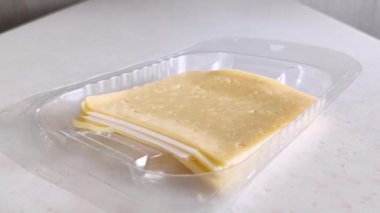 Plastik pakette sarı peynirin kare parçaları. Dişi beyaz el bir parça alır. İnek sütünden yapılmış küçük delikli dilimlenmiş peynir. Sandviç için hazır ürün. Yakın plan.