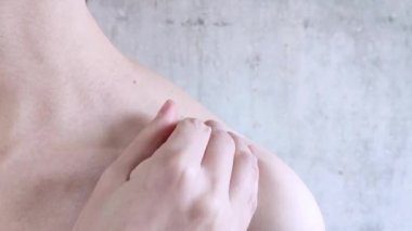 Beyaz kız omzuna bej sütyen takıyor. El sütyen ayarlıyor. Kadın iç çamaşırlarını giydirme süreci. Yakın plan. Beton duvar arkaplanı