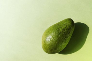 Avokado yeşil arka planda. Yatay afiş, fotokopi alanı olan poster. Sağlıklı organik yiyecekler. Tamamen doğal meyve. Vejetaryen konsepti. Sert güneş ışığı trendi, uzun gölge, tek renkli fotoğraf, düz yatış