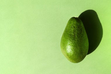 Kağıtlı arka planda yeşil Avokado. Doğa konsepti. Yatay poster, fotokopi alanı olan afiş. Tam çiğ meyve. Sağlıklı organik yiyecekler. Sert güneş ışığı eğilimi, uzun gölge, tek renk, düz yatış