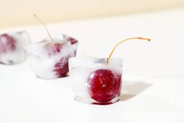 İçinde kiraz olan buz küpleri. Kış için vitaminlerin korunması. Dondurulmuş gıda şoku. Yaz meyvelerini tazeliyorum. Beyaz bej arka planda kırmızı kiraz.