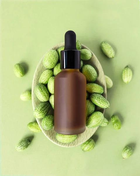 Vertical mockup of beauty oil bottle with black pipette cap on green background, exotic fruit. Frosted brown vial of emulsion, serum, extract. Natural herbal cosmetic. Organic design for spa, flat lay