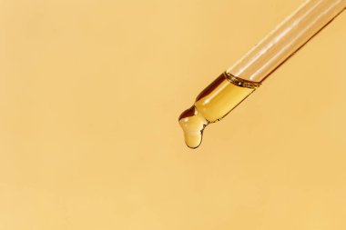 Petrol damlası dökülen bir boru. Losyonlu, özlü, serumlu, emülsiyonlu damlalar. Yatay tek renkli pankart, poster, fotokopi alanı, bej sarısı arka plan. Doğal organik kozmetik. Vücut bakımı kavramı