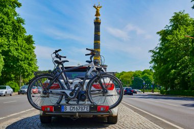 Berlin, Almanya - 8 Mayıs 2020: Arkasına bisiklet ve bisiklet monte edilmiş bir motosikletli park edilmiş araba. Arka planda odaklanmamış Berlin Siegessaeule 'ü görüyorsunuz, tarihi bir dönüm noktası..