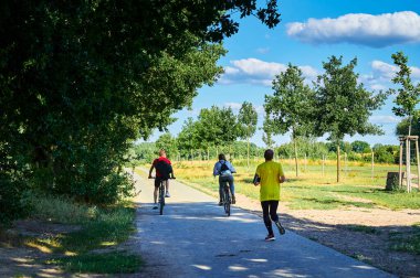 Grossziethen, Almanya - 21 Temmuz 2020: Spor giyimli bir koşucu ve Berlin Duvarı yolunda arkadan iki bisikletçi.