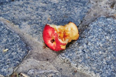 Bir caddenin kaldırım taşında duran ısırık bir elma manzarası.