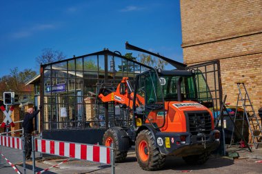 Berlin, Almanya - 9 Nisan 2020: Dresden demiryolu hattında inşaat alanı. Eski bir cam bisiklet kulübesini söken işçilere destek veren bir kazıcı görüyorsunuz..