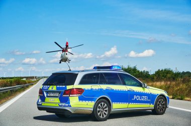 20. Otoyol, Almanya - 30 Ağustos 2020: Almanya 'da bir otoyol kurtarma operasyonu sırasında polis arabası ve helikopteri. Koyu noktalar, pervaneler tarafından tekmelenen toprak parçacıkları..