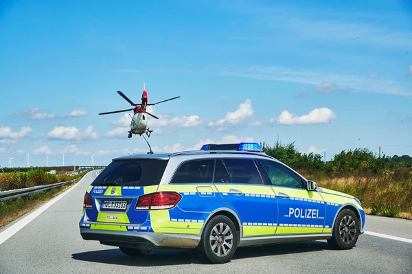 20. Otoyol, Almanya - 30 Ağustos 2020: Almanya 'da bir otoyol kurtarma operasyonu sırasında polis arabası ve helikopteri. Koyu noktalar, pervaneler tarafından tekmelenen toprak parçacıkları..