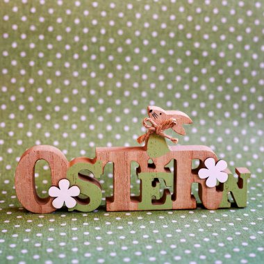 Yeşil arka planda beyaz noktalı bir Paskalya tavşanı olan tahta tabela. Metin Almanca Paskalya demektir..